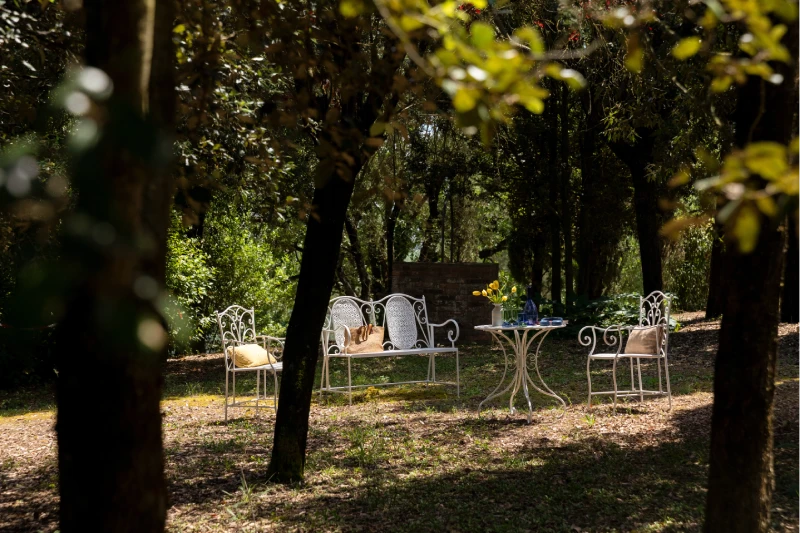 Shaded garden at the Villa Annex Adults Only with wrought-iron seating among the trees of the Crete Senesi - Castello di Leonina, BZAR hotels in Tuscany